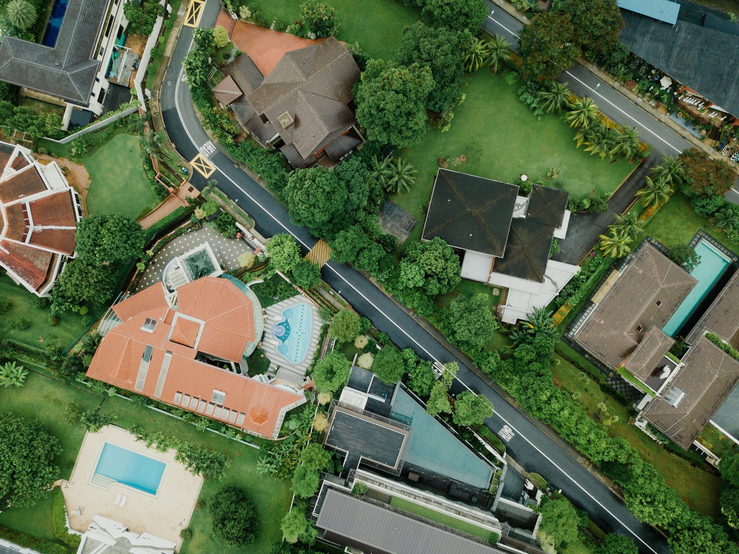 Aerial view of houses with pools and green lawns.