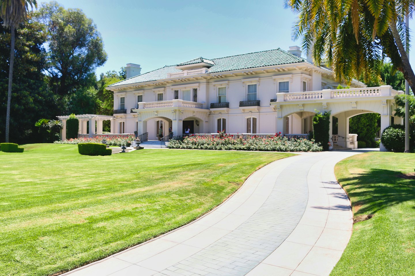 Grand white mansion with a red rose garden on a green lawn.